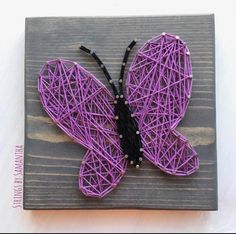 a purple string art butterfly sitting on top of a wooden board