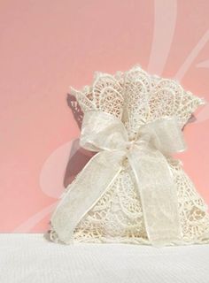 a white lace bag with a bow on the front and side, sitting against a pink background