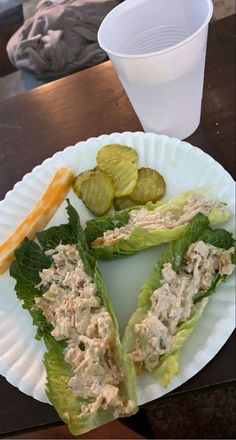 a white plate topped with lettuce and pickles next to a plastic cup