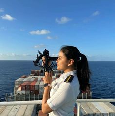 a woman holding a camera on top of a boat in the ocean next to a container ship