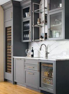 a kitchen with gray cabinets and marble counter tops, wine glasses on the cabinet doors