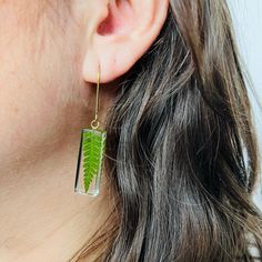 a close up of a person wearing earrings with a green leaf on it's ear