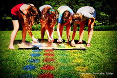 three girls are bending over on a skateboard in the grass with their hands together