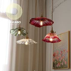 three lights hanging from a ceiling in a room with curtains and flowers on the window sill