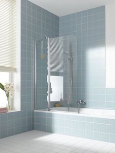 a bathroom with blue tiles and white fixtures, including a bathtub next to a window