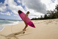 a woman holding a pink surfboard on top of a sandy beach