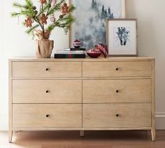 a wooden dresser with flowers and pictures on the top, in front of a white wall