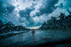 rain is falling on the windshield of a car as it drives down a road with trees in the background