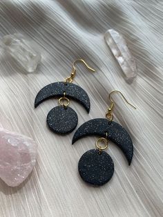 two black and gold moon earrings sitting on top of a white blanket next to crystals