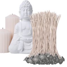 a white buddha statue sitting next to some candles and string wrapped in twine with beads