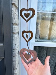 a hand holding a metal heart hanging from a chain with two hearts attached to it