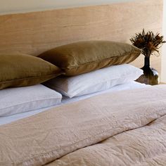 a bed with two pillows on top of it next to a vase filled with flowers