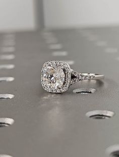 an engagement ring with a cushion cut diamond surrounded by smaller round diamonds on a metal surface