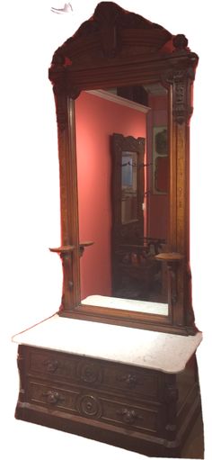 an ornate wooden mirror sitting on top of a bench in front of a pink wall