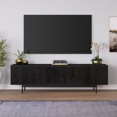 a living room with a large flat screen tv on the wall and plants in vases