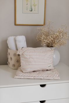 a white dresser topped with pillows and a vase filled with flowers