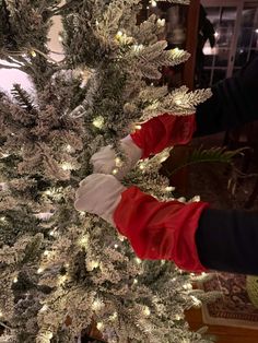 someone in red gloves is decorating a white christmas tree with silver and gold lights