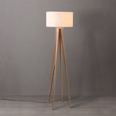 a wooden tripod floor lamp with a white shade on the top and a black cord attached to it