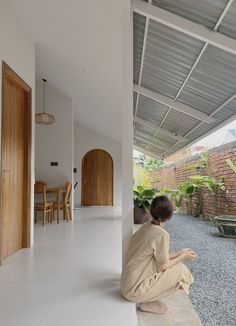 a woman sitting on the ground in front of a house with white walls and flooring