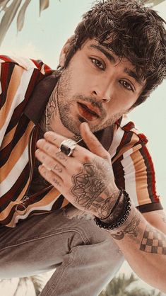 a man with tattoos on his arm posing for a photo in front of palm trees