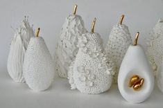 several white vases with gold handles are lined up against a white wall and one has an egg in the middle