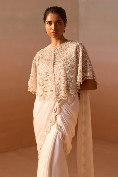 White poncho sleeves cape with all over scallop embroidery using silver nalki zircon and pearl highlights. Paired with a scallop embroidered border pre-draped saree with ruffled hem and a bustier. - Aza Fashions Embellished Blouse Piece With Traditional Drape For Wedding, Traditional Drape Embellished Blouse Piece For Wedding, Embellished Traditional Drape Blouse For Wedding, Traditional Drape Blouse With Dupatta For Wedding, Wedding Blouse With Traditional Drape And Dupatta, Traditional Drape Wedding Blouse With Dupatta, Traditional Wedding Blouse With Dupatta, Wedding Embellished Pre-draped Saree, Transitional Season Embellished Wedding Saree