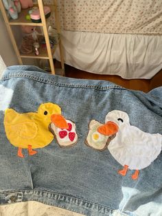 two little chickens and one big chicken are sitting on someone's jeans in front of the bed