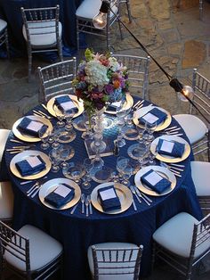 the table is set with blue and gold plates, silver chairs, and flowers in vases