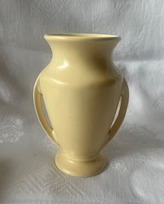 a yellow vase sitting on top of a white cloth