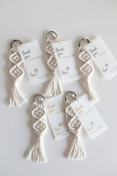 four white tasselled key chains with tags attached to them on a white surface