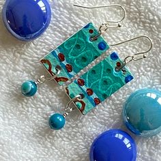 two blue and one green earrings are on a white blanket next to each other,