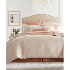 a bed with pink comforter and pillows in a room next to a chandelier