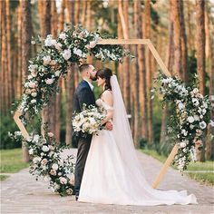 a bride and groom standing in front of an arch decorated with white flowers at their wedding