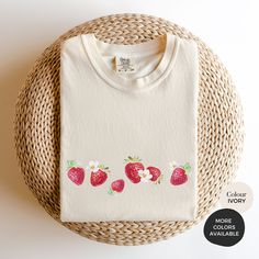 a white t - shirt with strawberries painted on the front and back, next to a wicker basket