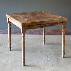 a wooden table with two legs and a square top on the floor in front of a gray wall