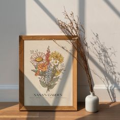 there is a vase with some flowers in it next to a framed print on the wall