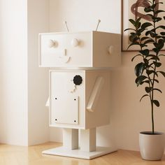 a white robot sitting on top of a wooden floor next to a potted plant