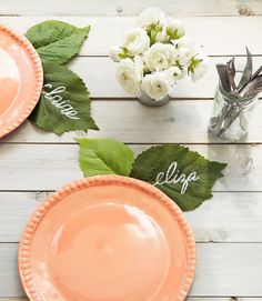 two orange plates sitting on top of a wooden table next to white flowers and greenery