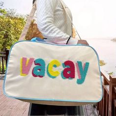 Description: Get ready for your next adventure with the VACAY Travel Bag. Features a vibrant and playful design with the word "VACAY" in colorful letters. Spacious interior, perfect for packing all your travel essentials. 9”W x 12”H x 20.5”L Material & Care: Fabric: Durable and lightweight polyester blend. Care Instructions: Wipe clean with a damp cloth. Do not bleach. Handle with care to maintain the vibrant colors. Playful Rectangular Travel Luggage, Playful Rectangular Luggage For Travel, Trendy Travel Bag With Luggage Sleeve For School, Trendy School Travel Bag With Luggage Sleeve, Retro Travel Bag With Large Capacity, Travel Tote Shoulder Bag With Letter Print, Multicolor Shoulder Bag With Luggage Sleeve For Trips, Trendy White Travel Bag, Trendy Multicolor Bags For Weekend Trips