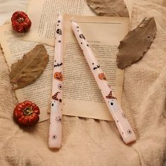 two bookmarks with leaves and pumpkins on top of an open book next to some dried leaves