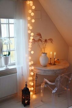 a white table and chair in a room with lights on the wall above it, next to a window