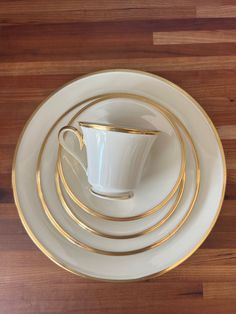 a stack of white and gold plates on top of a wooden table next to a cup