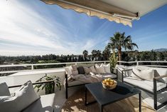 an outdoor living area with couches, tables and chairs on a balcony overlooking the trees