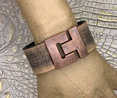 I spend a great deal of time searching for unique jewelry and bag components. Combining vintage finds with new results in many one-of-a-kind pieces. Striking 1-1/8" wide heavy leather cuff bracelet features distressed taupe brown buffalo leather strap. Heavy leather strap is 3mm (about 1/8") thick. It keeps its shape. 33mm tall matte antique copper plated zinc toggle clasp has magnetic for extra security. Size 7-1/2". Hand crafted! Thank you for visiting - message me if you have a question. Buff Adjustable Bracelet With Antique Finish, Unique Adjustable Bracelets With Antique Finish, Unique Adjustable Bracelet With Antique Finish, Adjustable Brown Jewelry With Antique Buckle, Brown Rectangular Vintage Bracelet, Vintage Brown Metal Cuff Bracelet, Unique Brown Metal Cuff Bracelet, Vintage Bronze Cuff Jewelry, Vintage Brown Jewelry With Antique Buckle