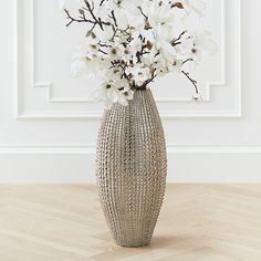 a vase filled with white flowers sitting on top of a wooden floor next to a wall