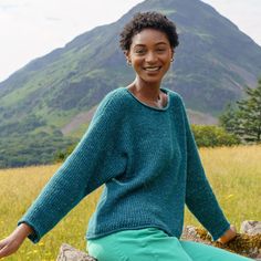 a woman sitting on top of a rock in front of a green field and mountain