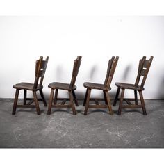 three wooden chairs sitting next to each other on a cement floor in front of a white wall