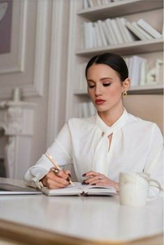 a woman sitting at a desk writing on a book and holding a pen in her hand