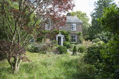 an old brick house surrounded by trees and bushes in the country side yard with lots of green grass