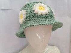 a green crocheted hat with white and yellow flowers on the brim, sitting on a mannequin head